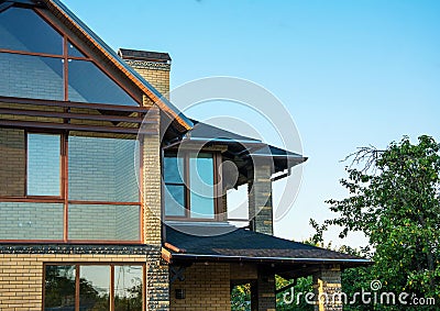 Brick house with panoramic windows, multilevel roof, glazed facade, chimney with forging, closeup. Stock Photo