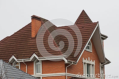 Brick house with white windows and brown tiled roof with chimneys Stock Photo