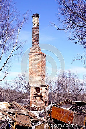 Brick oven with a pipe from the burnt house. Ruins after the fire of a wooden house. High pipe from the furnace against the blue s Stock Photo