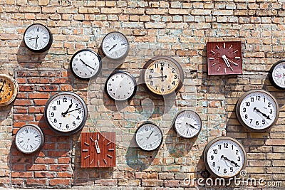 Brick wall background with numerous round and square clocks. Stock Photo