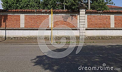 Brick wall with columns and lower side made of bricks. Porphyry sidewalk, yellow pole and asphalt street in front. Stock Photo