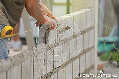 bricklayer hands hold aluminium brick trowel installing brick blocks on construction site Stock Photo