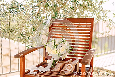 Bridal bouquet of white roses, freesia, boxwood branches and white ribbons near the shoes of the bride on the wooden Stock Photo