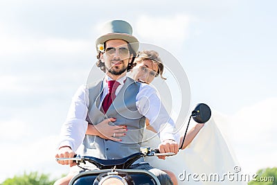 Bridal pair driving motor scooter wearing gown and suit Stock Photo