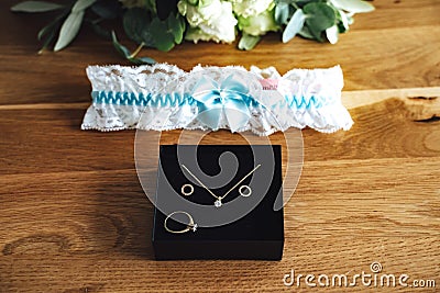 Bride accessories: black jewelry box with golden ring, necklace and earrings on wooden board. White lace garter with Stock Photo
