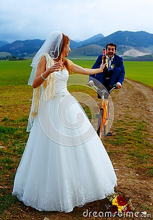 Bride with a beer bottle and a groom on bicycle on the background - wedding concept. Stock Photo