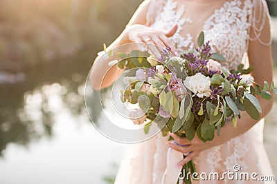 The bride in a beige wedding dress touching a lush bridal bouquet of lilac roses and a lot of greenery. Stylish wedding bouquet on Stock Photo