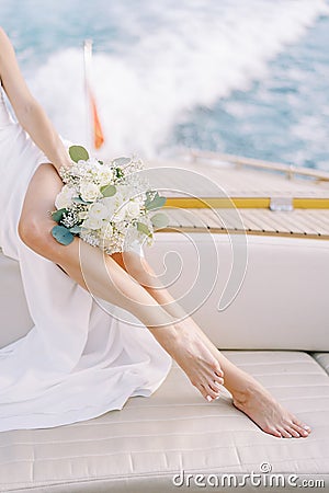 Bride with a bouquet sits on board a yacht sailing on the sea. Cropped. Faceless Stock Photo