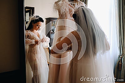 the bride, dressed in a boudoir transparent dress and underwear, stands at home in the morning by the mirror Stock Photo