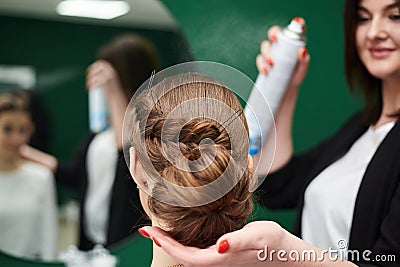 Bride getting ready for wedding. Professional hairdresser making coiffure for female client, applying hairspray in front of big Stock Photo