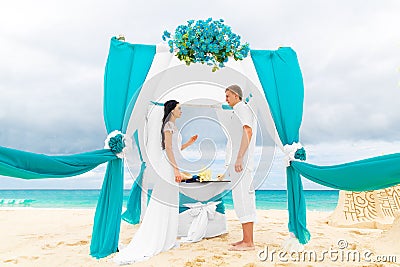 Bride giving an engagement ring to her groom under the arch decorated with flowers on the sandy beach. Wedding ceremony on Stock Photo