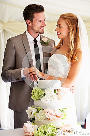 Bride And Groom Cutting Wedding Cake At Reception Stock Photo