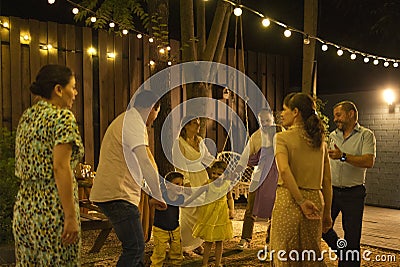 Bride and groom dancing first dance in front of best friends and kids, relatives and guests at illuminated backyard Stock Photo