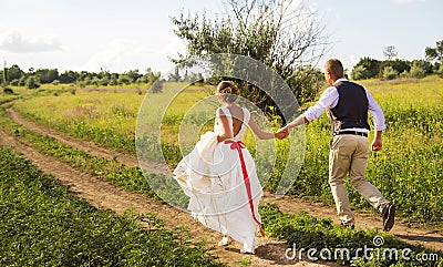 The bride and groom happily run along the path in the park. The groom holds the bride`s hand. Stock Photo