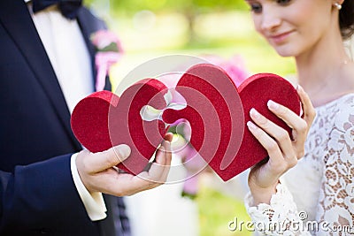 Bride and groom holding red puzzle hearts, wedding concept, closeup Stock Photo