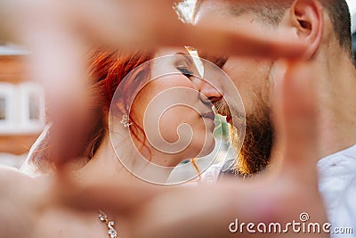 The bride and groom kissing while making a frame with their hands Stock Photo