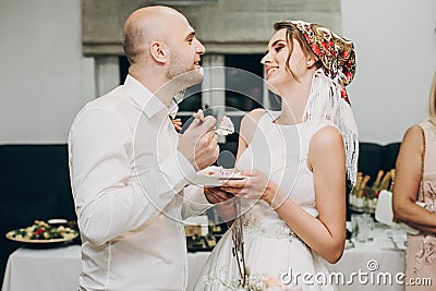 Bride and groom tasting wedding cake at wedding reception in restaurant. Wedding couple plate with slice of cream cake decorated Stock Photo