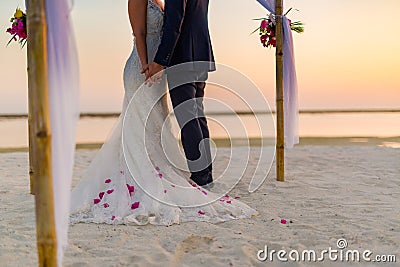 The bride and groom under archway on beach. Calm and romantic white sandy beach for honeymoon destination and love background Stock Photo