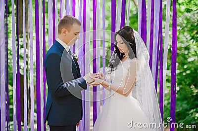 The bride and groom wear each other at a wedding ceremony when rings on a background of multi-colored ribbons, love, marriage, rel Stock Photo