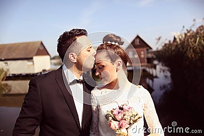 Bride and groom on wooden bridge near houses on lake Stock Photo