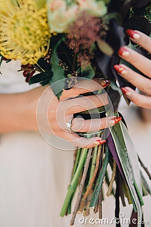 Bride hand with beautiful red manicure and a luxury ring with diamonds is holding a wedding bouquet. Close-up Stock Photo