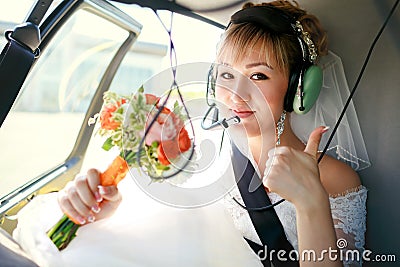 Bride inside helicopter preparing to fly, in headset, thumbs up. Stock Photo