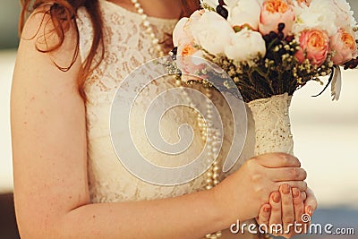 Bride in pearls holds a wedding bouquet decotated with lace Stock Photo