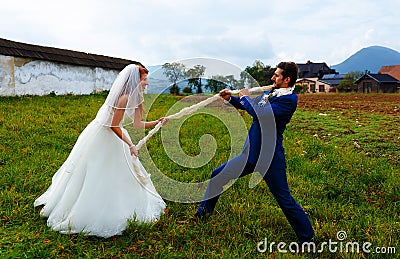 Bride pulling her groom to her with a rope - funny wedding concept. Stock Photo