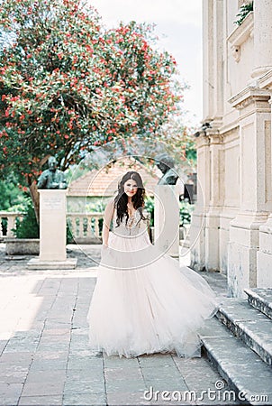 Bride stands near the steps of a stone building against the backdrop of a flowering tree Stock Photo