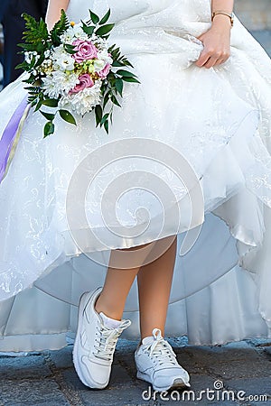 Bride with a wedding bouquet dressed in white dress showing sneakers on her legs Stock Photo