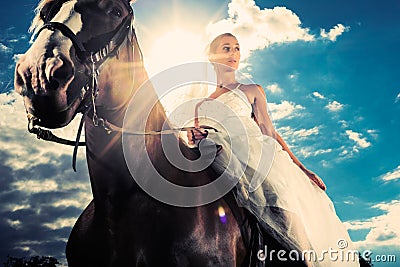 Bride in wedding dress riding a horse, backlit Stock Photo