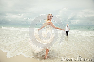 Bride in wedding dress runs to bridegroom over sea turning back. lucky woman on the beach. Stock Photo