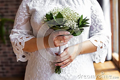 Bride in a white dress standing and holding a wedding bouquet of white gypsophila, close up. Stock Photo