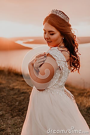 Bride in white wedding dress with a crown on her head stands on cliff against the background of the river and islands Stock Photo