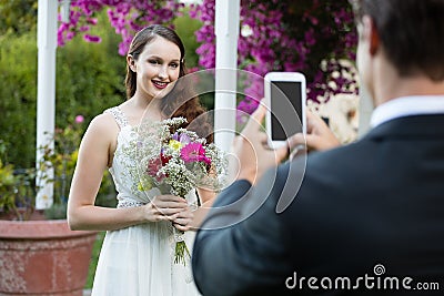 Bridegroom photographing bride holding bouquet at park Stock Photo