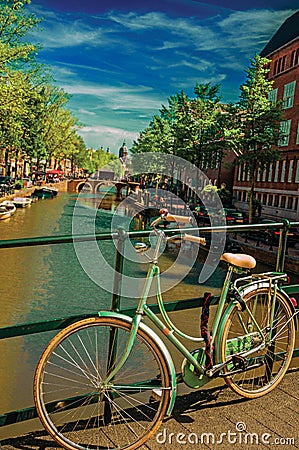 Bridge on canal with bike stuck at balustrade and moored boats under blue sky in Amsterdam. Stock Photo