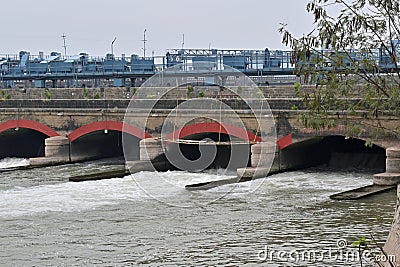 Bridge with multiple red-arched structures spanning a river, facilitating controlled water flow beneath. Stock Photo