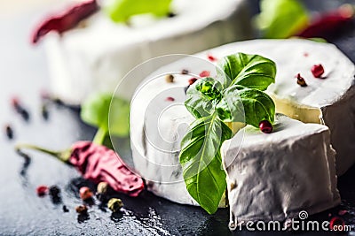 Brie cheese. Camembert cheese. Fresh Brie cheese and a slice on a granite board with basil leaves four colors peper and chili pepe Stock Photo