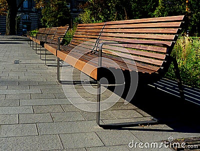 Bright brown wooden park benches in diminishing perspective with green landscape Stock Photo