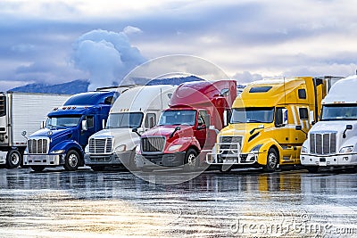 Bright colorful big rigs semi trucks with semi trailers standing in the row on truck stop parking lot at early morning Stock Photo