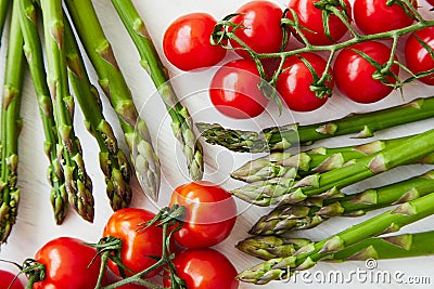 Bright and colorful flat lay composition of asparagus stems and branches of cherry tomatoes on a white rustic table. Stock Photo