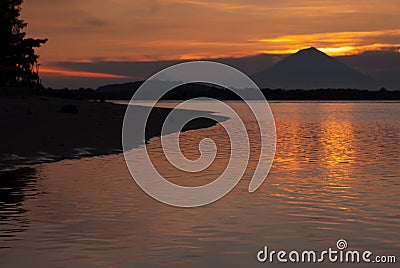 Bright colorful sunset on sea with golden sky and last sunbeams, dark volcano on horizon on distance island, calm orange water. Stock Photo