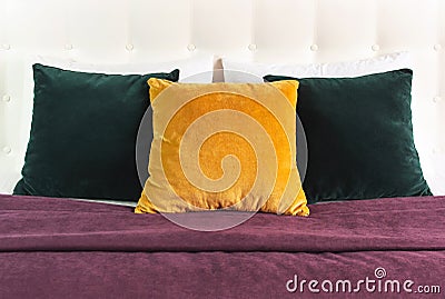 Bright decorative soft pillows in bed on the background of leather quilted headboard. Emerald and orange pillow, part of bed close Stock Photo