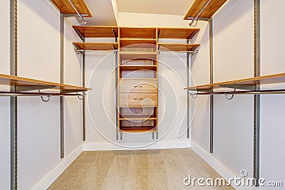 Bright empty walk-in closet with wood shelves, beige carpet floor. Stock Photo