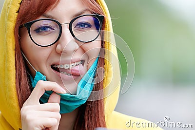 A bright girl with glasses and braces joyfully removes the medical mask from her face, mimics and shows her tongue Stock Photo