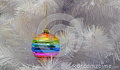 Bright glass rainbow colored Christmas ball, bauble hanging on a white artificial christmas tree. Copy space. The concept of the Stock Photo