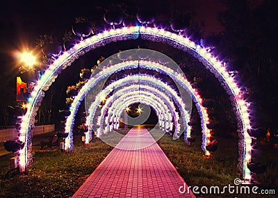 Bright glowing arch of colored lanterns in the park in the evening Stock Photo