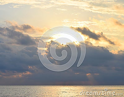 Bright Golden Yellow Sunlight from Dark Grey Clouds in Sky spreading over Ocean with Reflection in Water - Skyscape Stock Photo