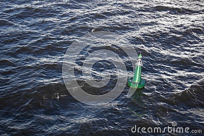 Bright green signal buoy in the dark blue sea among the waves Stock Photo