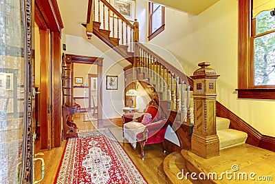 Bright hallway with colourful rug, nice red sofa, wooden staircase and beige carpet covered steps Stock Photo